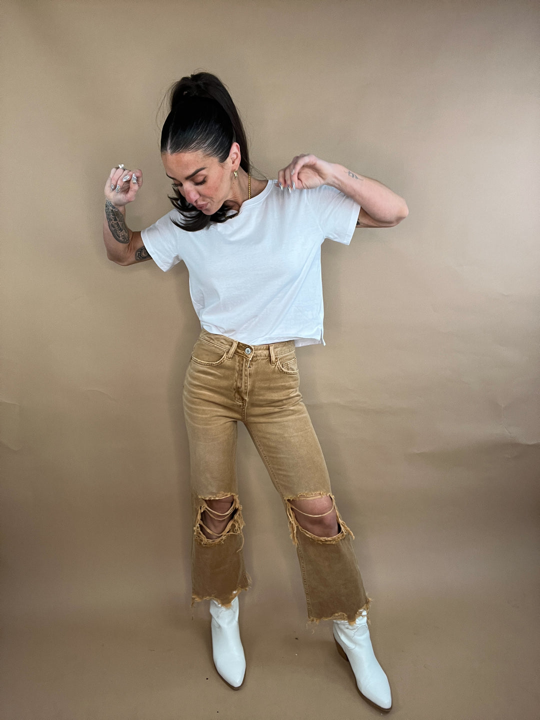 Tan denim pants with distressed detailing through the knees and a raw hem stiff leg denim with mid rise fit
